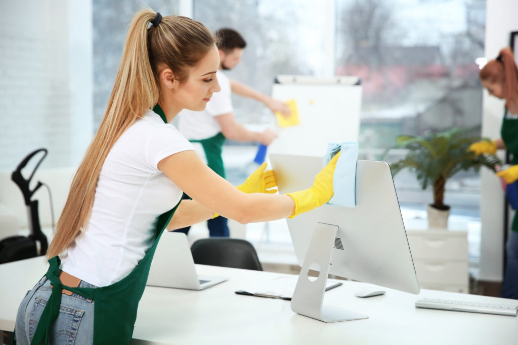 Jeune femme en gants de ménage nettoie l'écran d'un bureau