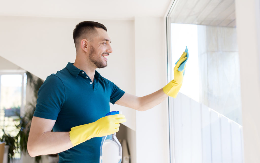 Jeune homme en gant de ménage nettoie une vitre